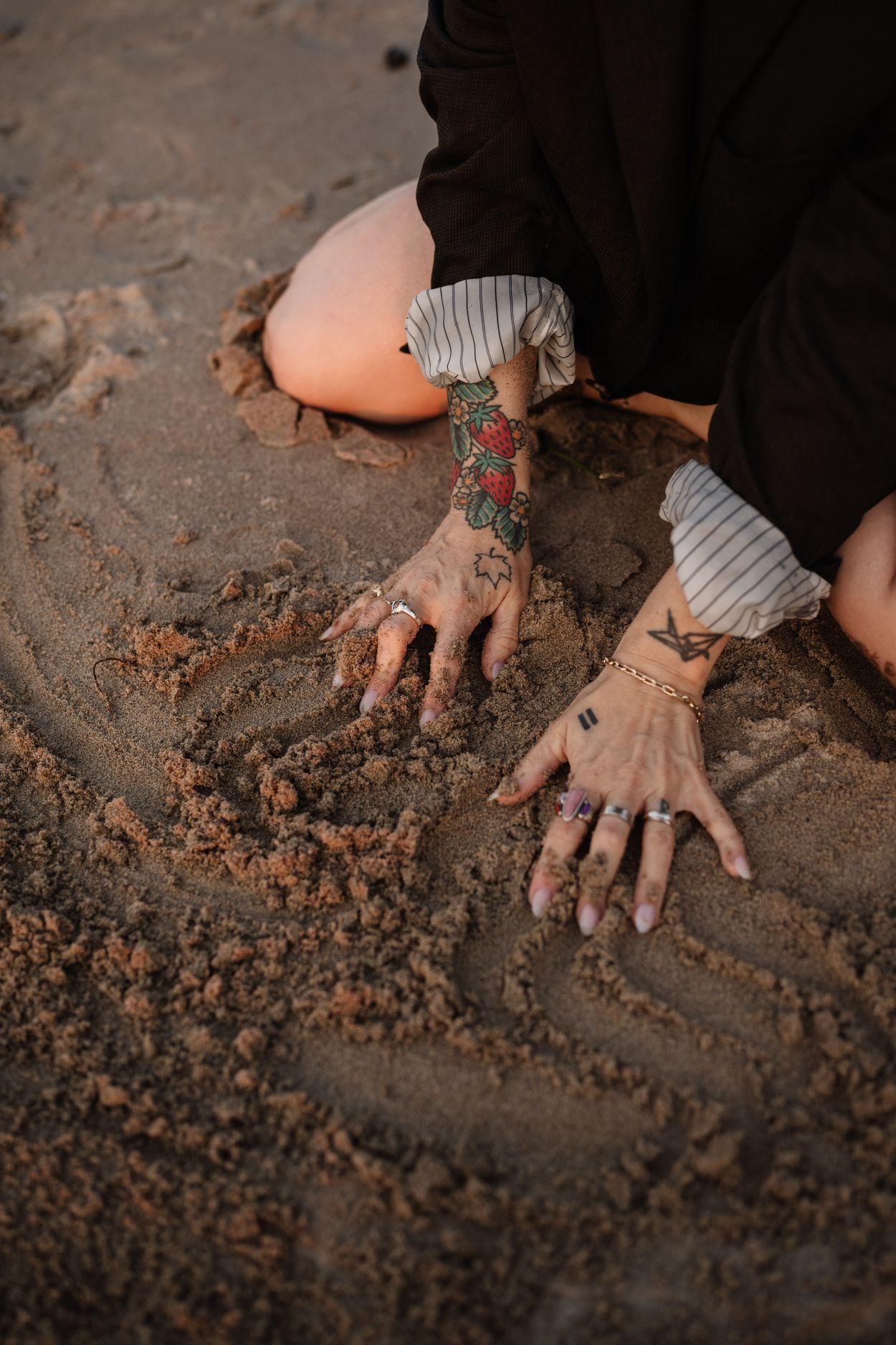 Two tattooed hands pressed into wet sand at the shoreline.
