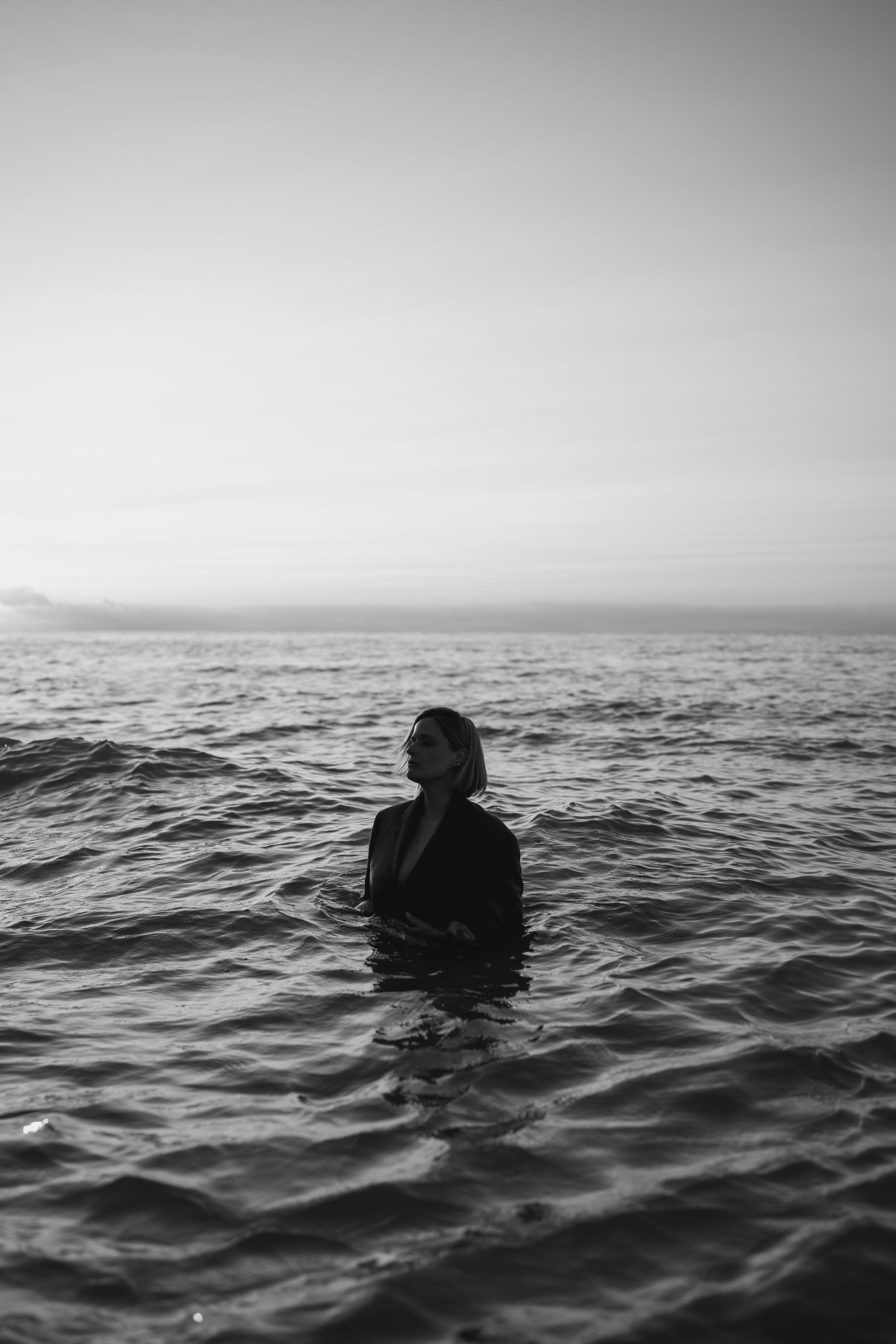 Meg standing waist-deep in open water at dusk, looking out toward the horizon.